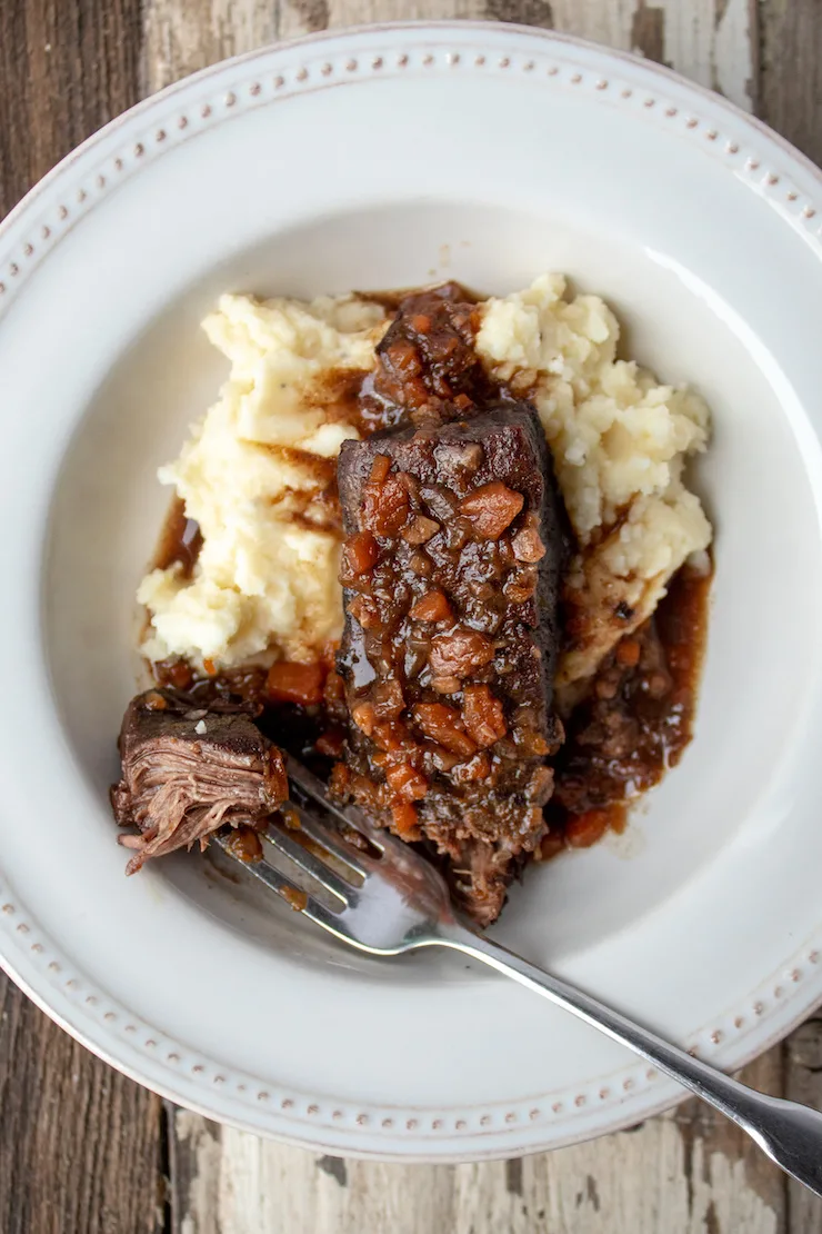 Short ribs plated with mashed potatoes and sauce, showing forkful of beef.