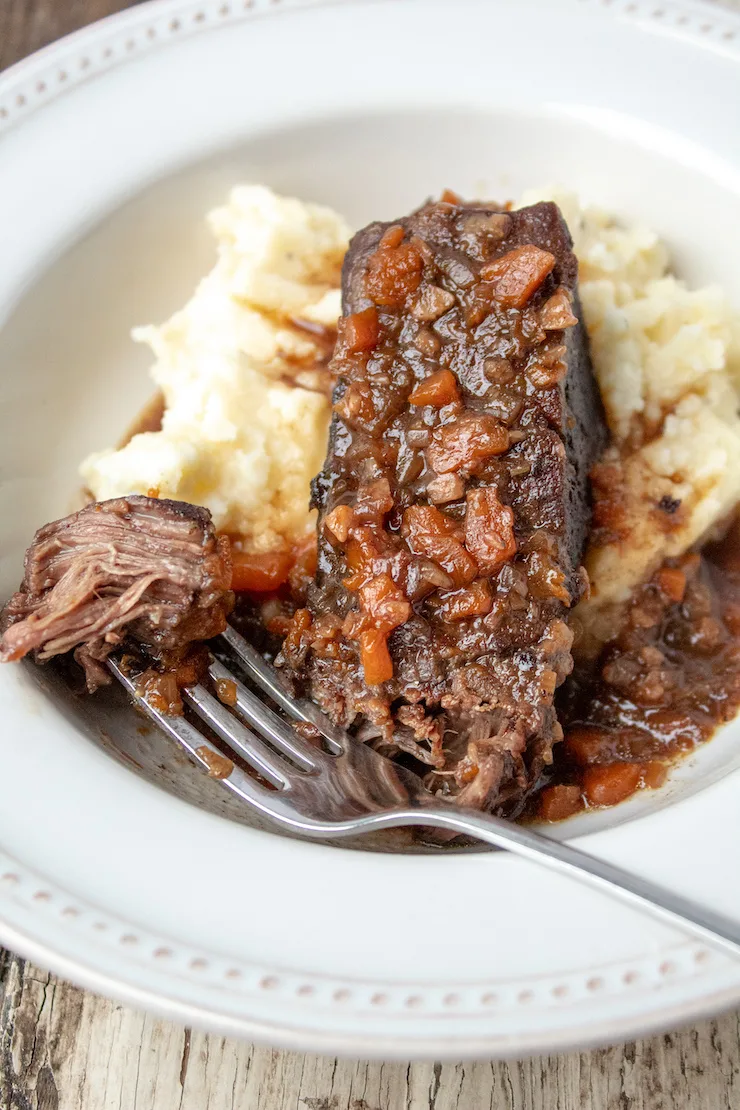 Instant Pot braised short ribs in bowl with mashed potatoes, forkful of meat on side.