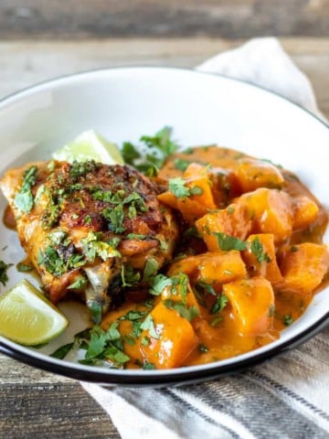 Curried sweet potatoes and skillet chicken on serving plate with lime wedges.