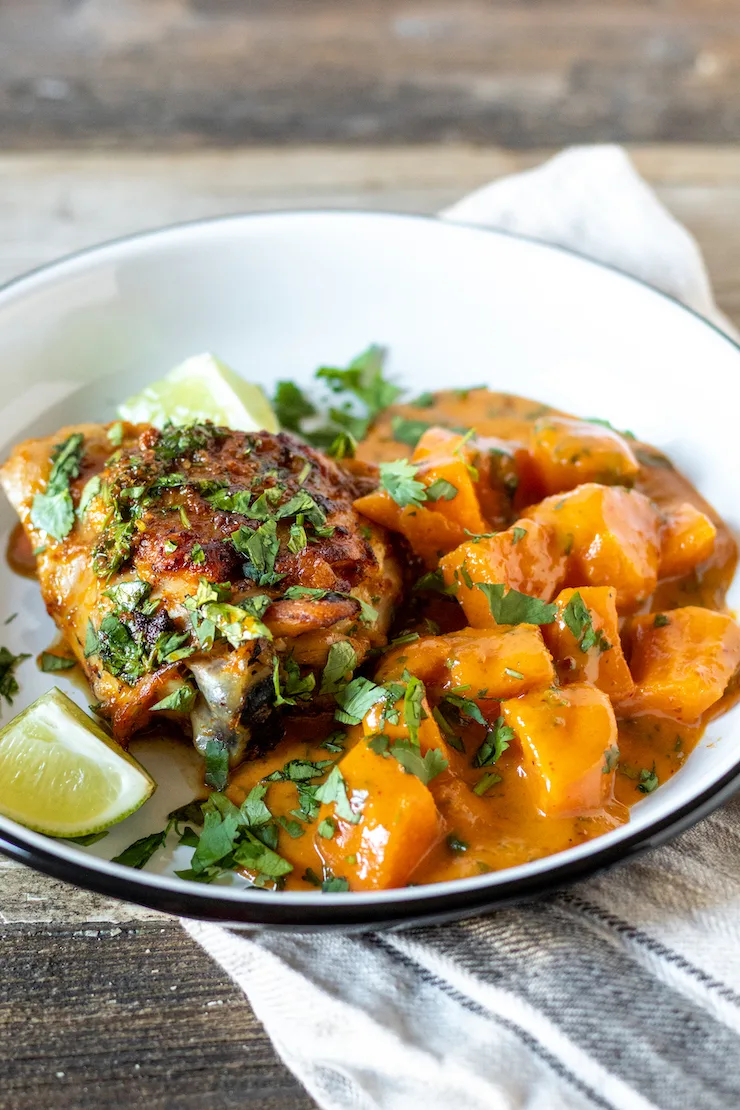 Curried sweet potatoes and skillet chicken on serving plate with lime wedges.