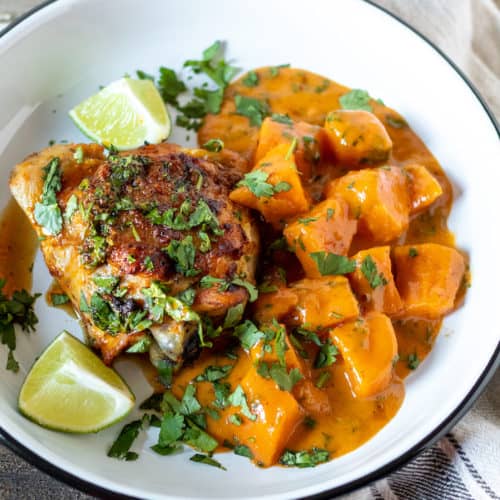 Sweet Potato curry with chicken thigh on plate garnished with lime and cilantro.