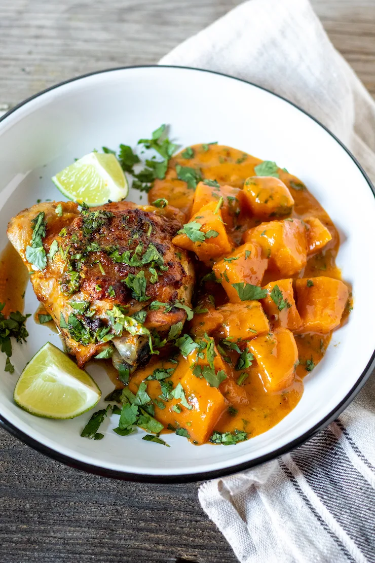 Sweet Potato curry with chicken thigh on plate garnished with lime and cilantro.