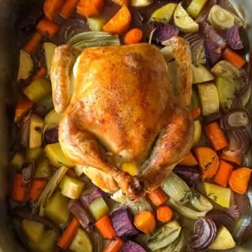 Roasted chicken over vegetables in roasting pan.