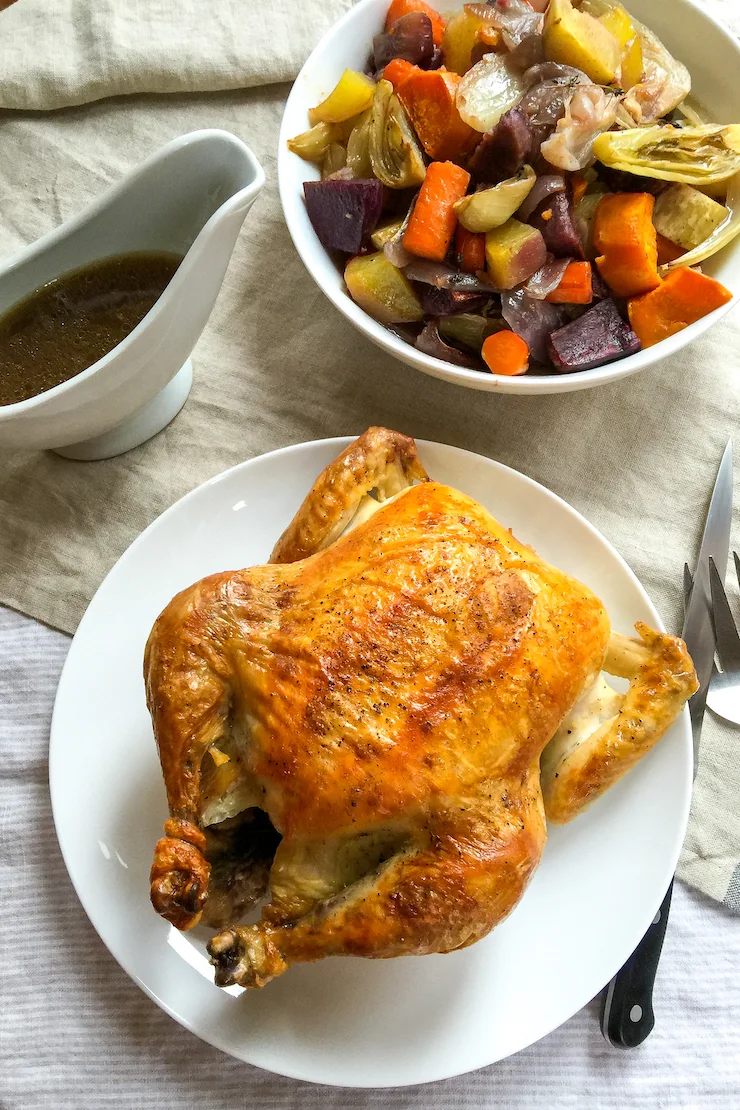 Roast chicken on tables with vegetables and pan juices.