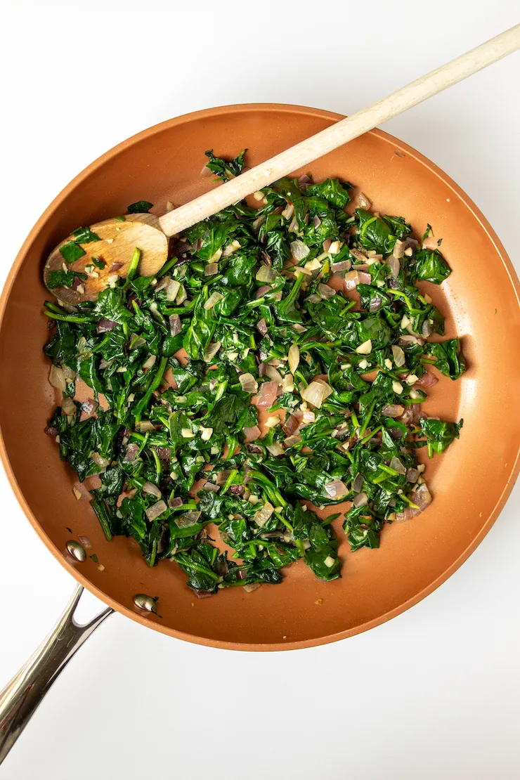 Sautéed spinach with garlic and onion in skillet.
