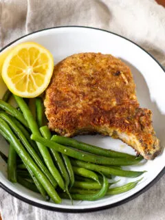 Breaded pork chop plated with green beans and lemon.