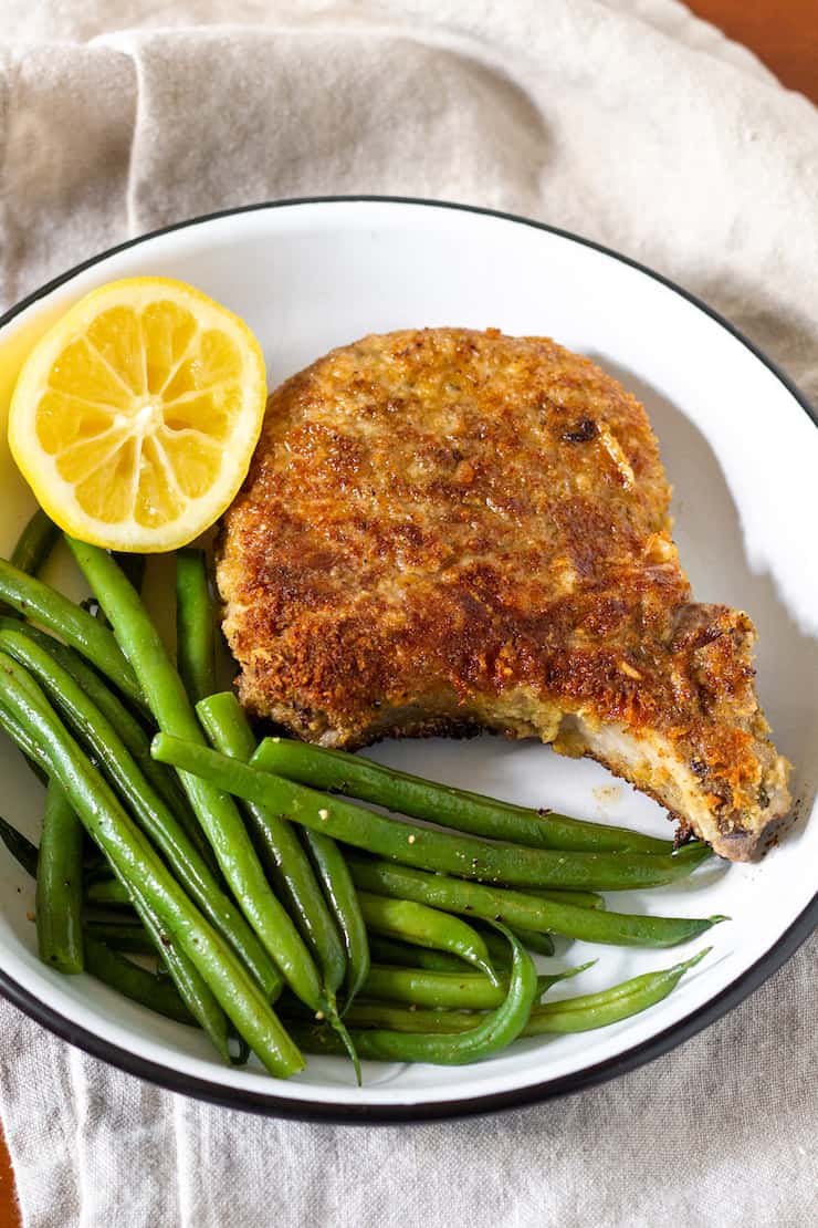 Breaded pork chop plated with green beans and lemon.