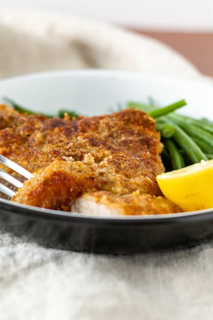 Breaded pork chop on serving dish with piece on a fork.