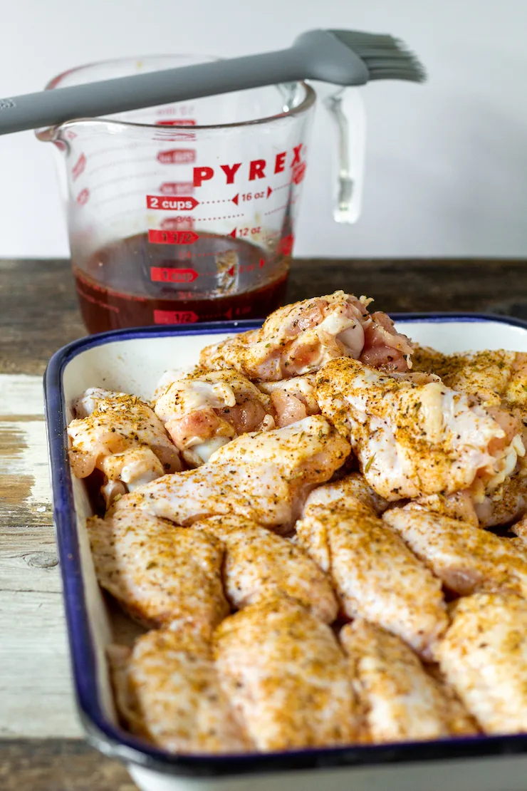 Seasoned chicken wings with sauce and brush in background.