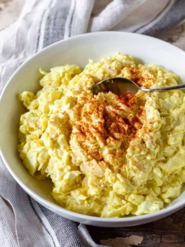 Finished potato salad in bowl with spoon and aprika.
