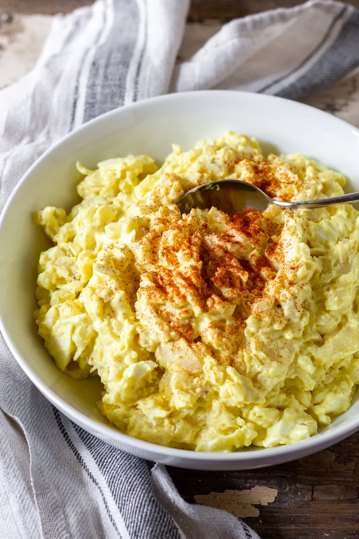 Finished potato salad in bowl with spoon and aprika.