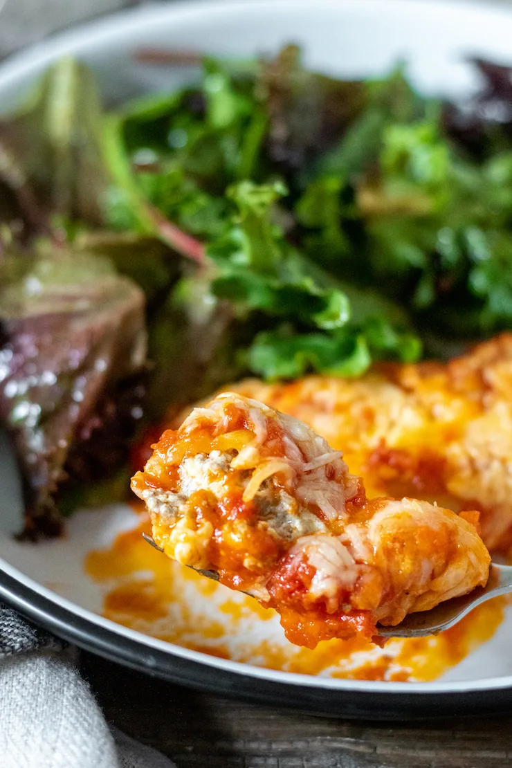 Plated manicotti shown with forkful and salad in background.