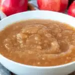 Instant Pot applesauce in white serving bowl, surrounded by apples in background.