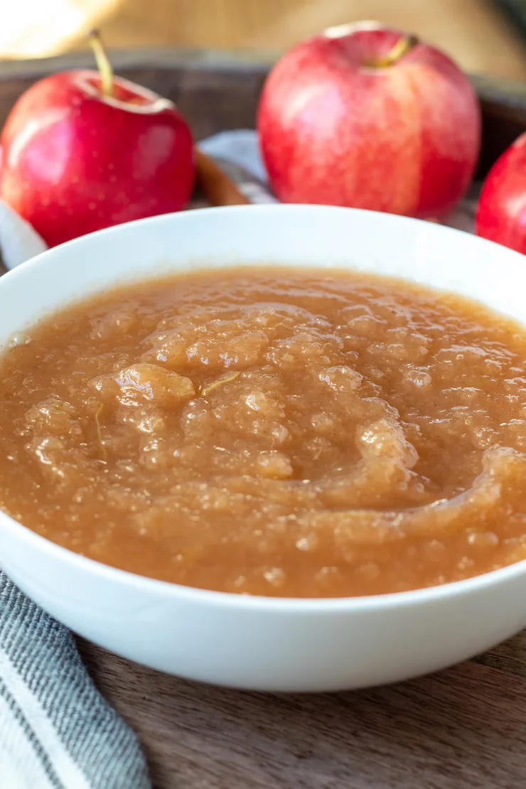 Instant Pot applesauce in white serving bowl, surrounded by apples in background.
