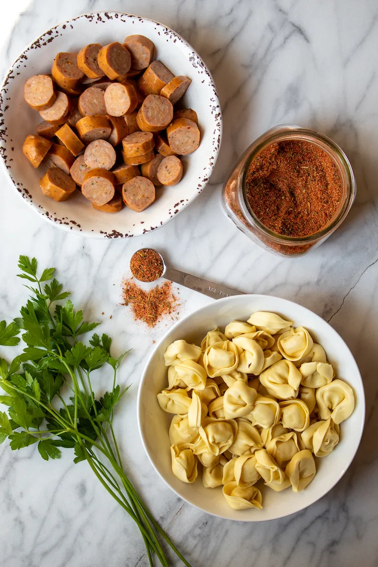 Close up of tortellini, sausage and homemade Cajun seasoning on marble board.