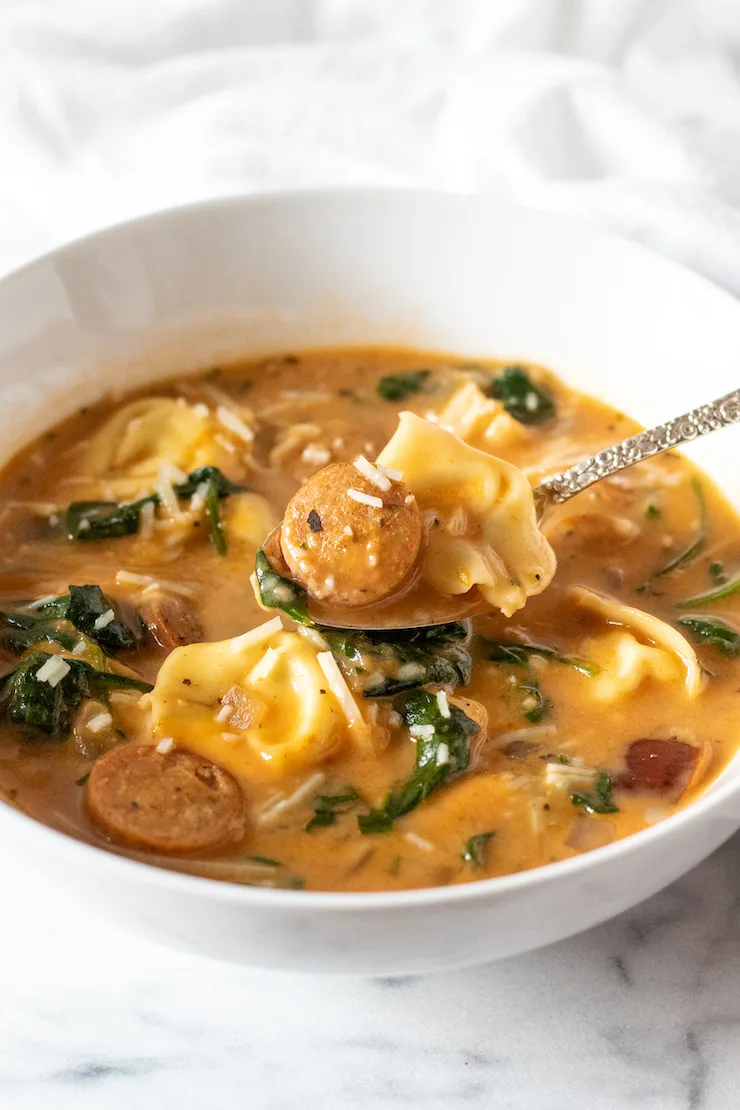 Creamy Cajun soup with tortellini and sausage on spoon.