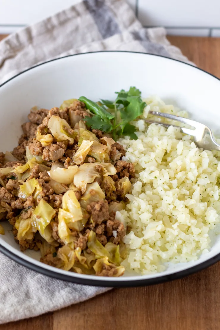 Pork cabbage stir-fry plated with cauliflower rice.