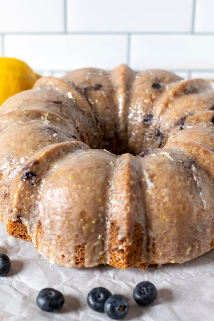 Glazed blueberry lemon cake with blueberries and lemon in background.