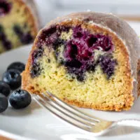 Close up of slice of cake on plate with fork and blueberries.