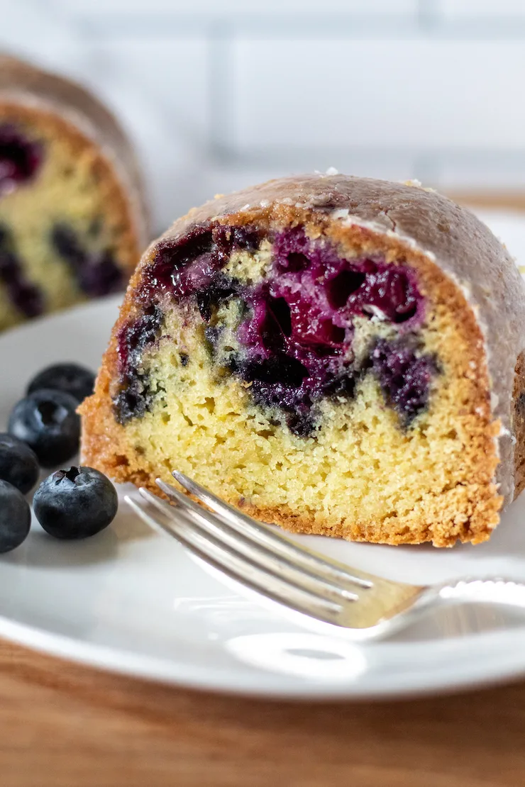 Close up of slice of cake on plate with fork and blueberries.