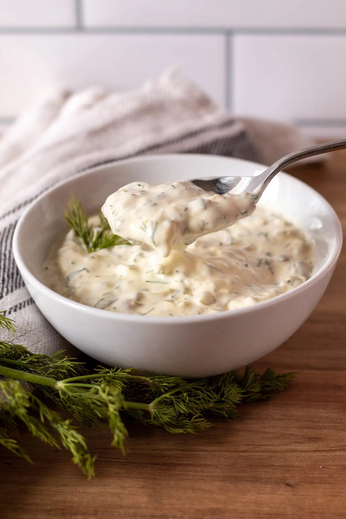 Homemade tartar sauce in white bowl, spoonful above bowl.