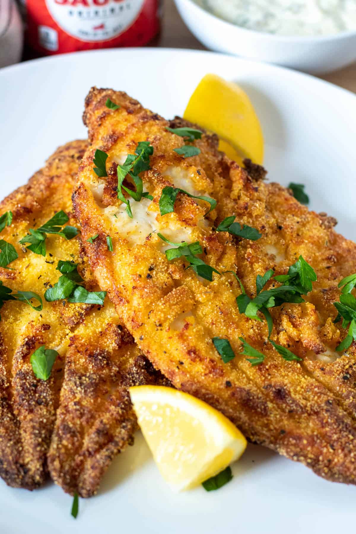 Two air crispy golden air fryer catfish fillets on plate with lemon wedges.