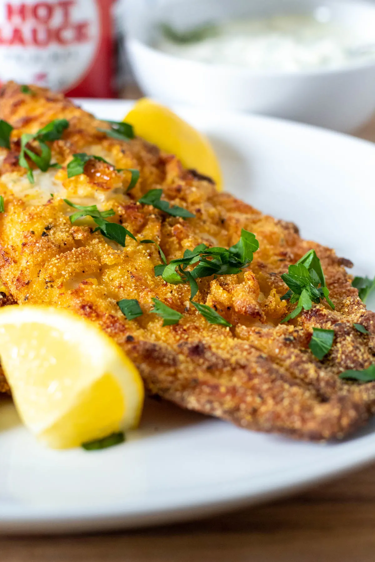 Up close air fryer catfish with lemon wedges and hot sauce in background.