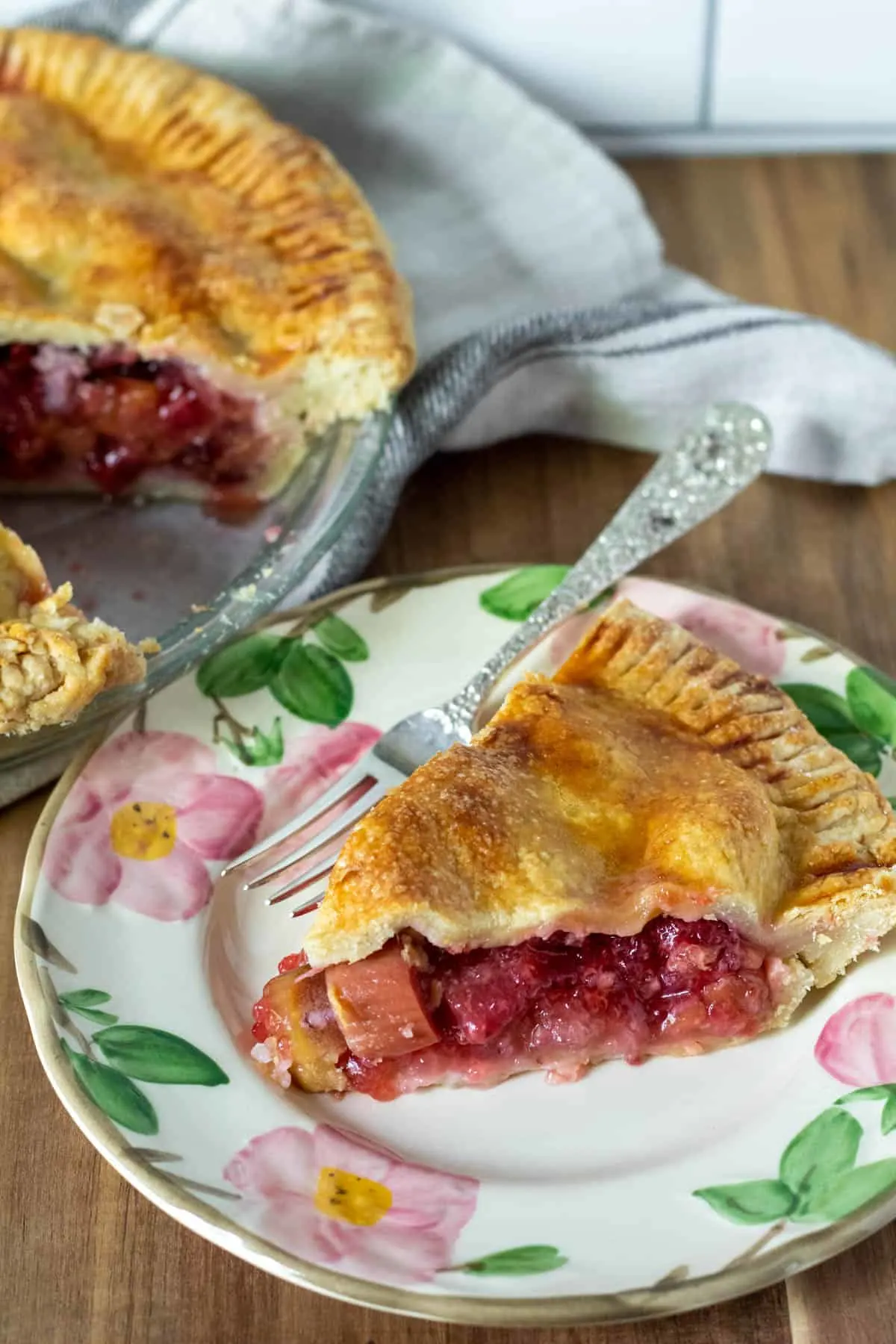 Pie on serving plate with whole strawberry rhubarb pie in background. 