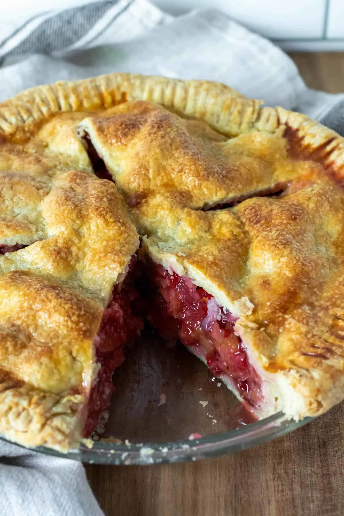 Close up of strawberry rhubarb pie with one piece cut out showing filling in crust.