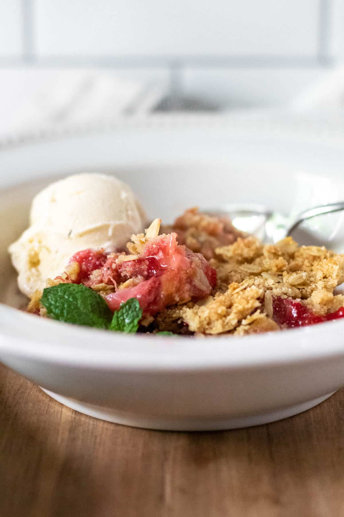 Strawberry rhubarb crisp in bowl with ice cream.