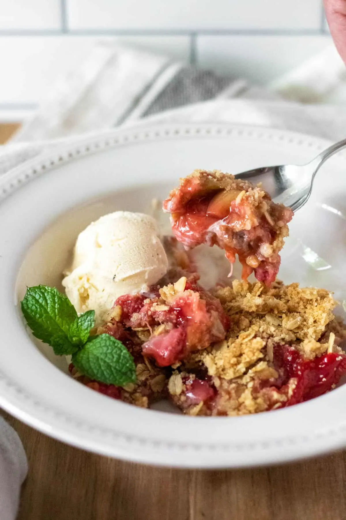 Spoonful of strawberry rhubarb crisp coming out of bowl with scoop of ice cream.