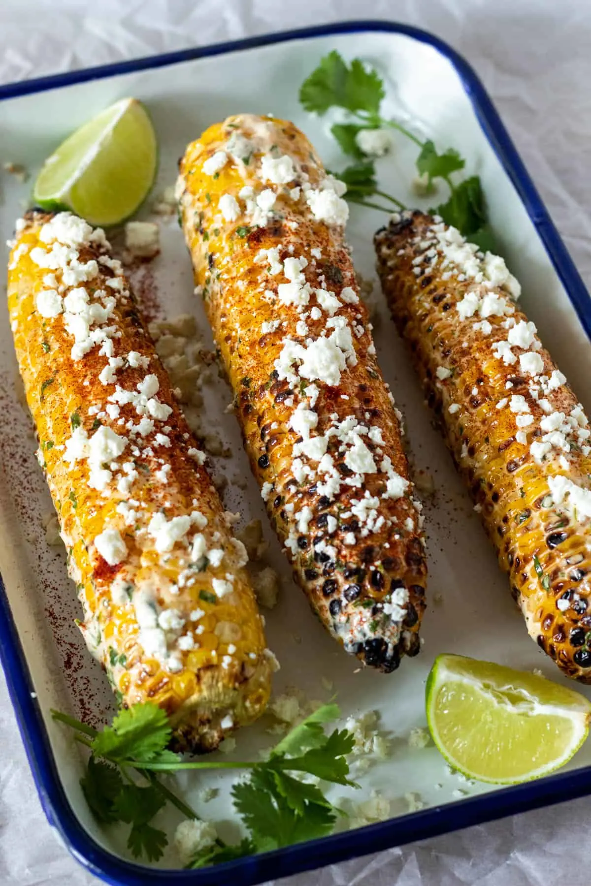 Grilled Mexican corn on serving platter with cream sauce and crumbled cheese.