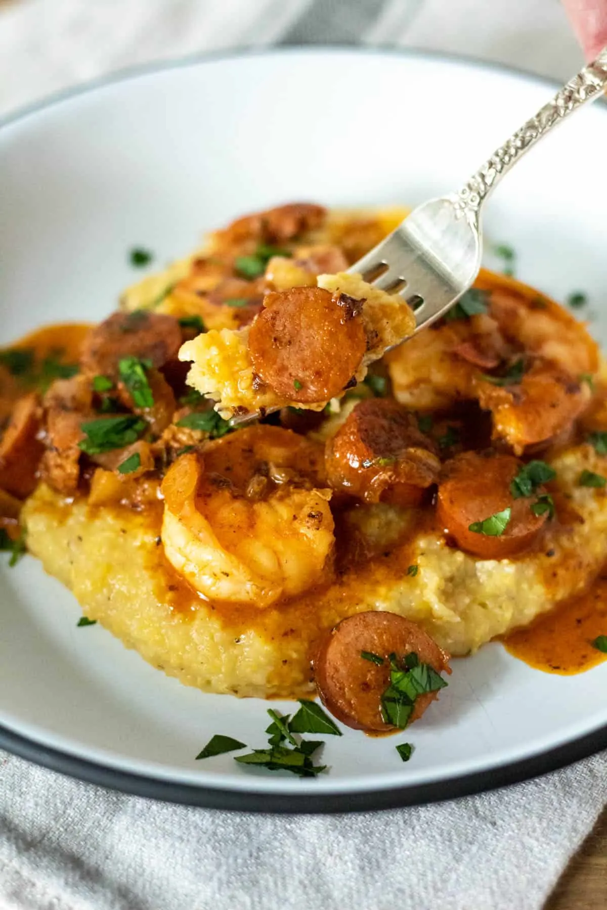 Shrimp and grits on plate with forkful of sausage and grits.