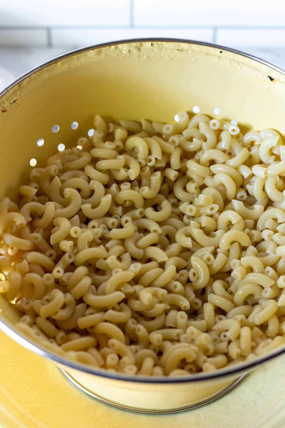 Cooked macaroni draining in yellow colander.