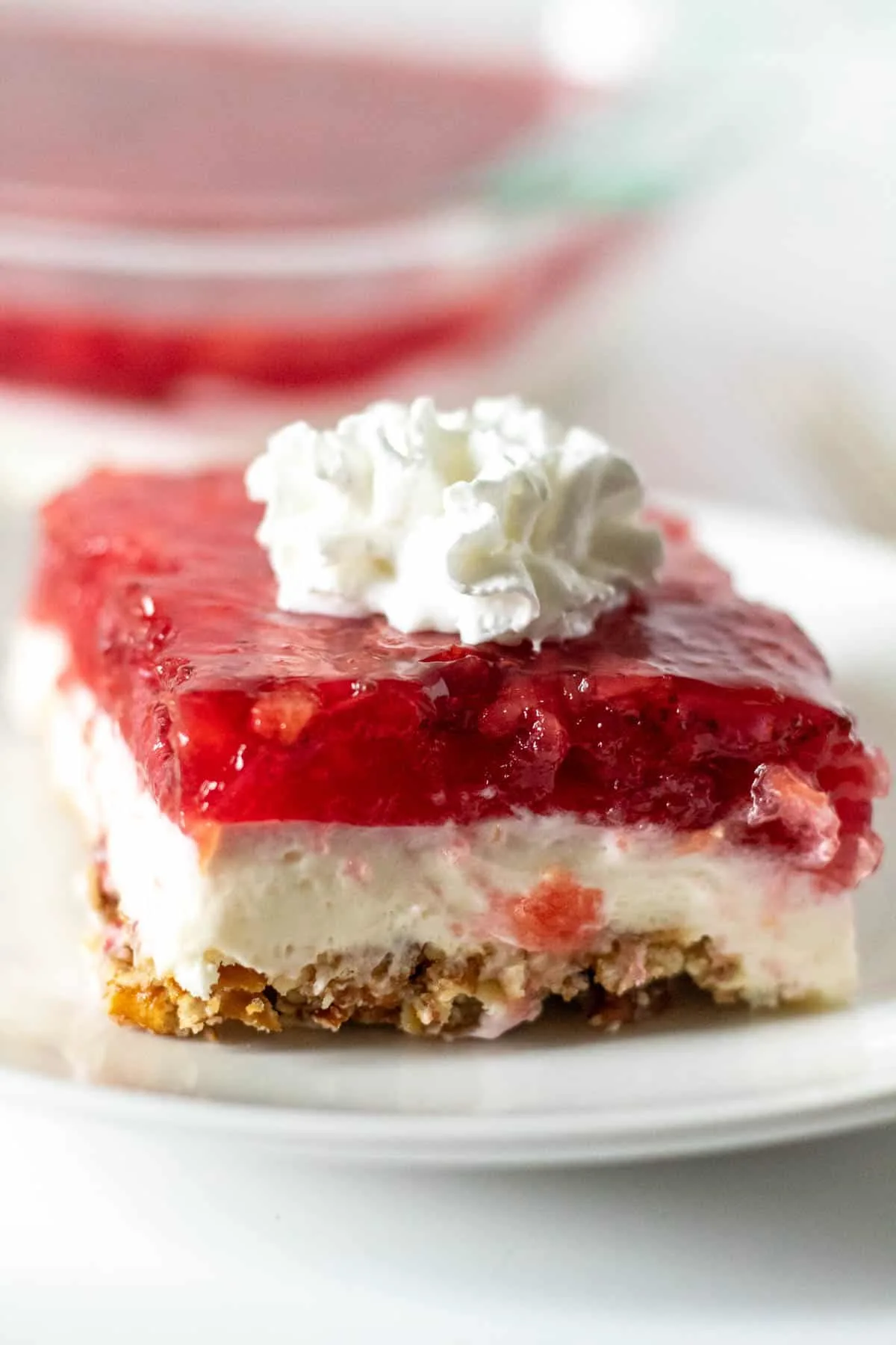 Slice of strawberry pretzel salad with whipped cream on top.
