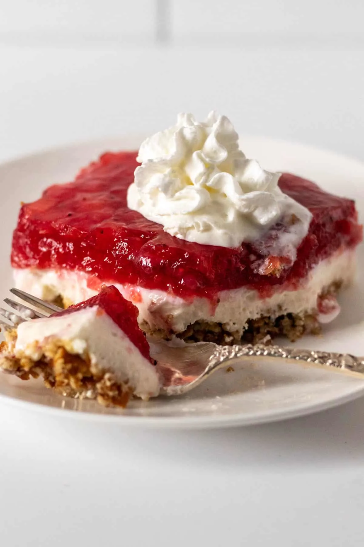 Piece of strawberry pretzel salad with forkful resting on white plate.