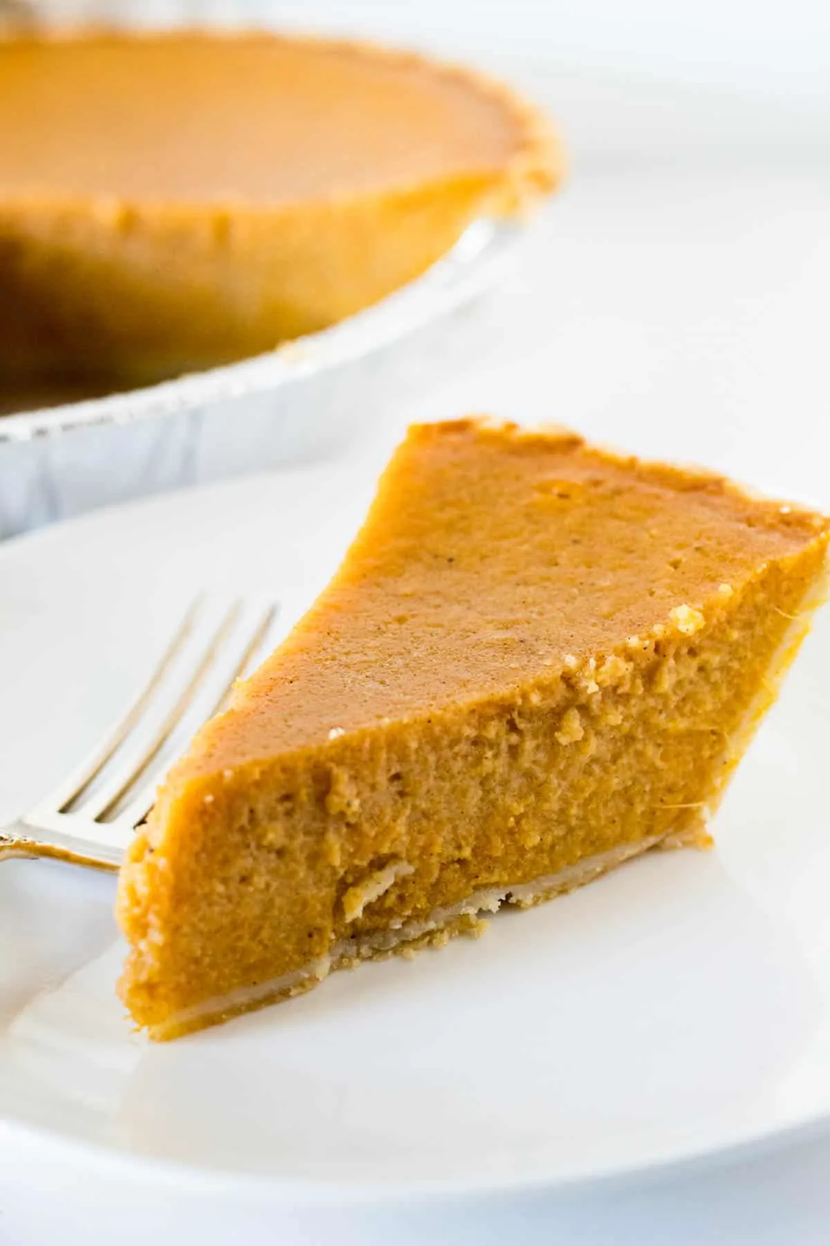 Piece of pie on white plate with whole pie in background.