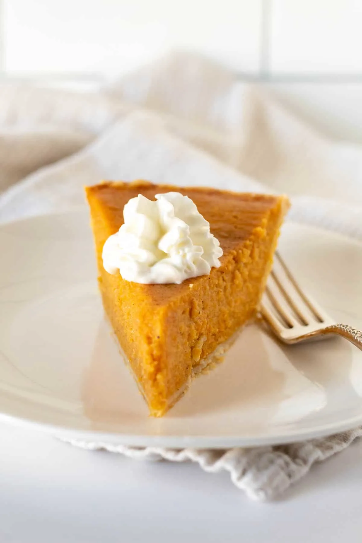 Front view of slice of sweet potato pie with whipped cream and fork.