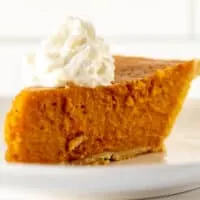 Close up of slice of sweet potato pie with dollop of whipped cream on white plate.