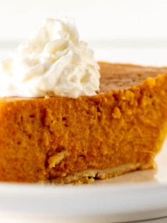 Close up of slice of sweet potato pie with dollop of whipped cream on white plate.