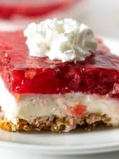 Close up of piece of strawberry pretzel dessert with dollop of whipped cream on top.