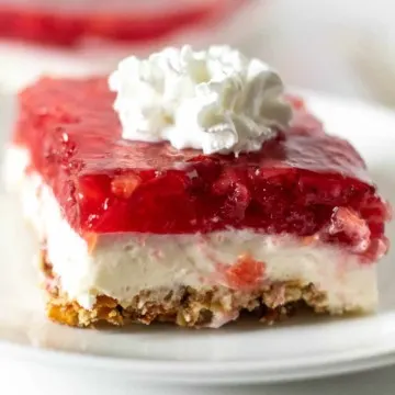 Close up of piece of strawberry pretzel dessert with dollop of whipped cream on top.