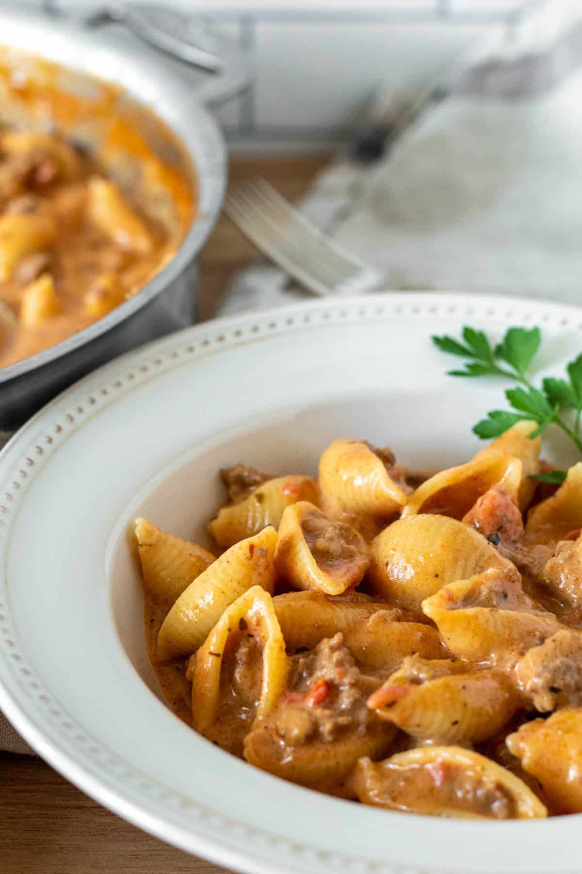 Bowl of cheesy beef and pasta shells with skillet in background.