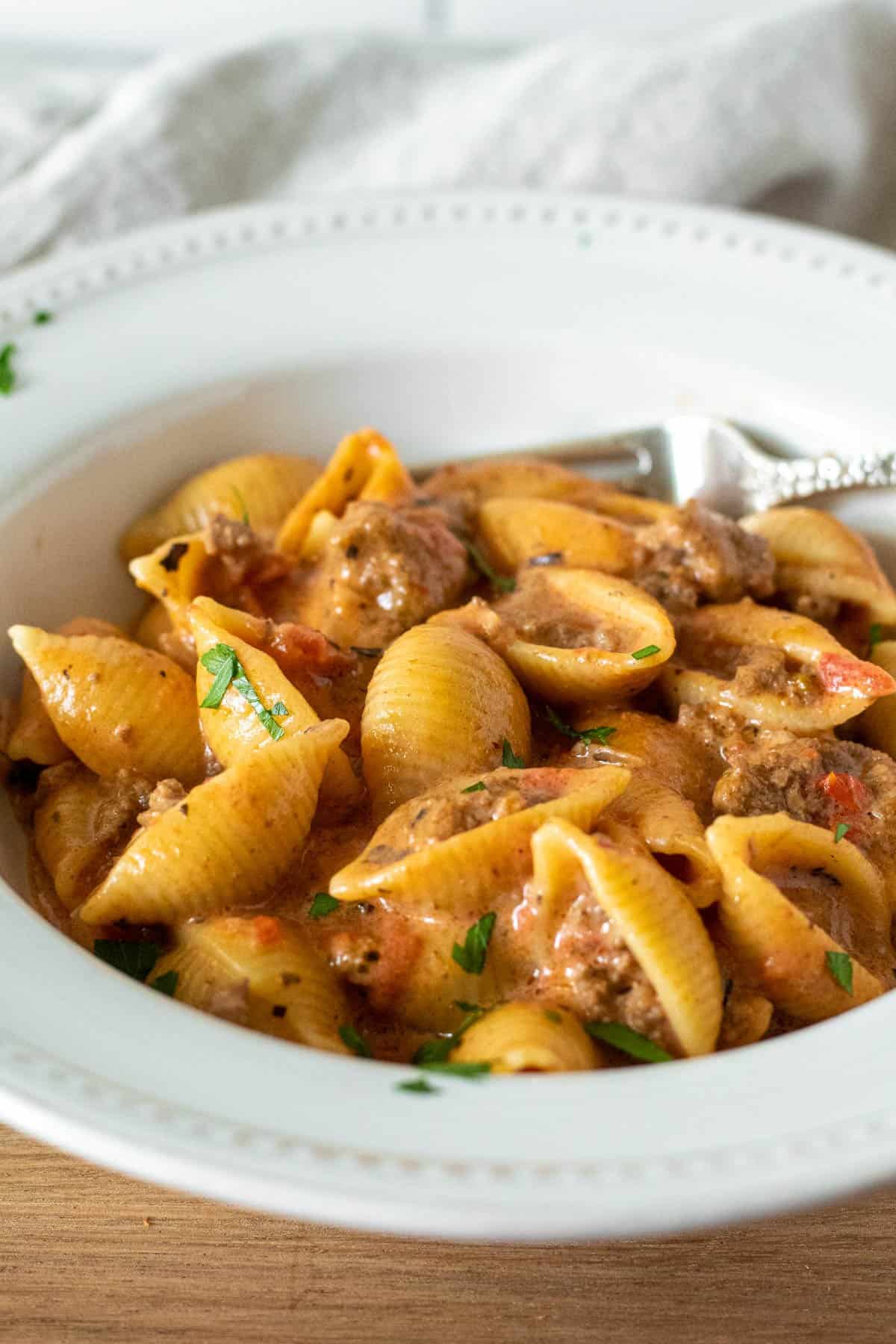 Bowl of cheesy beef pasta shells with fork.