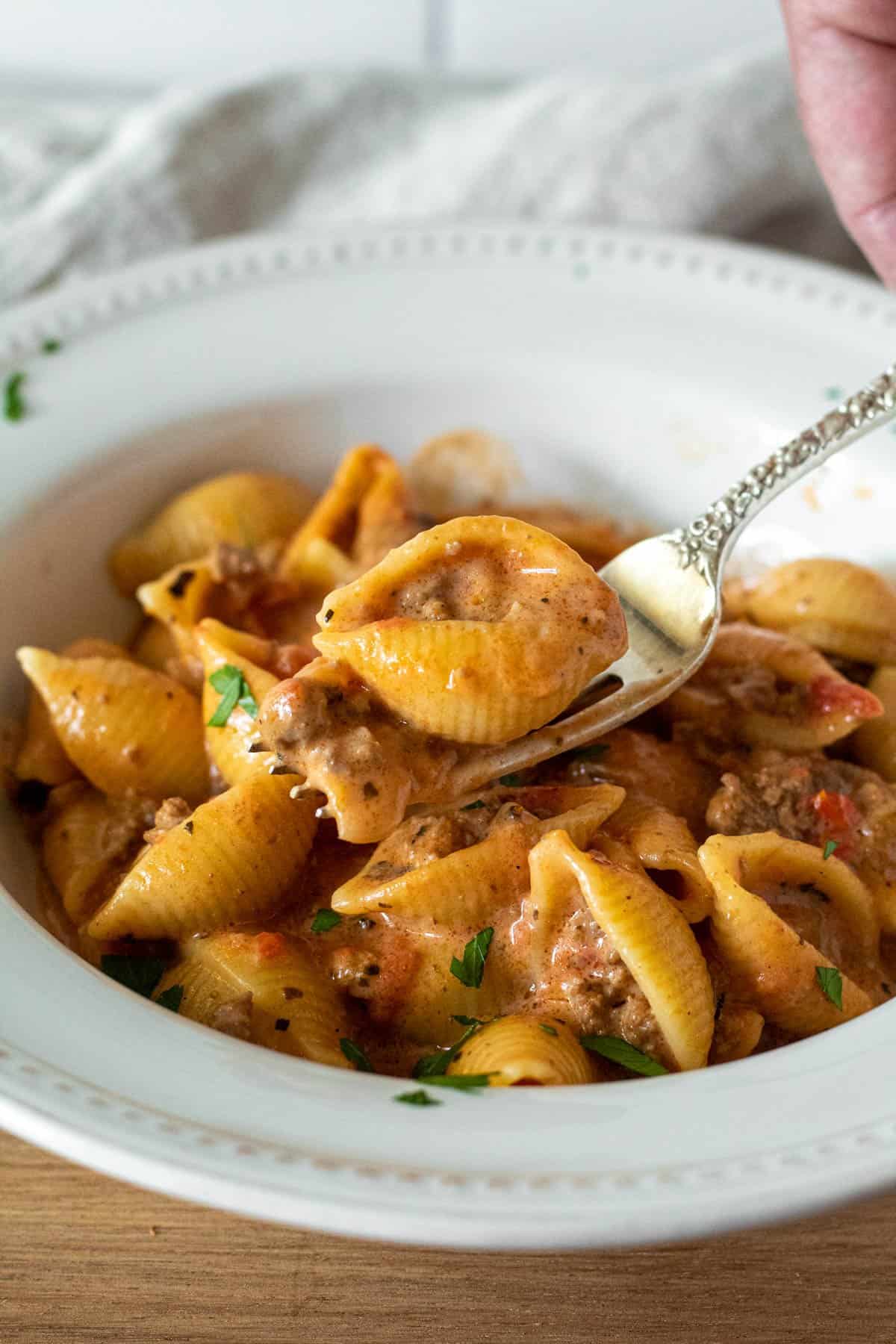 Bowl of cheesy beef pasta with shell on a fork.