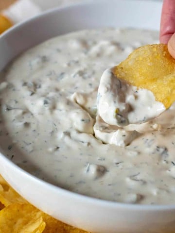 Hand scooping dill pickle dip with a potato chip.