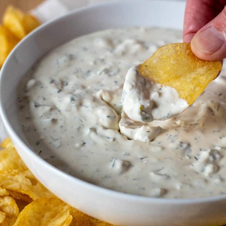 Hand scooping dill pickle dip with a potato chip.