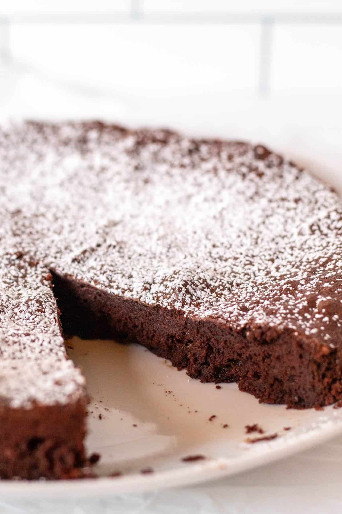 Whole bitterswweet chocolate cake with powdered sugarr and pice cut out.