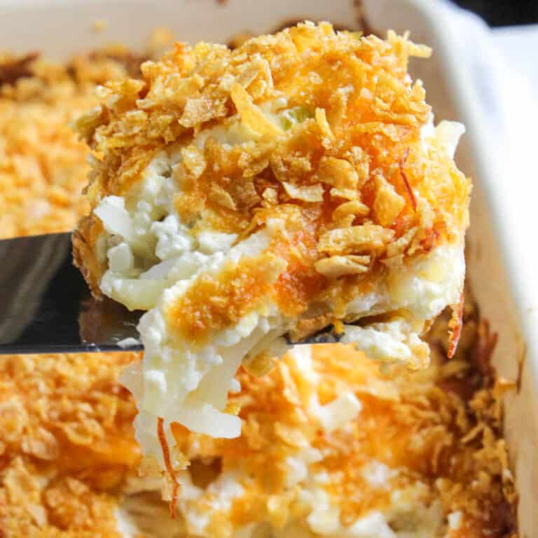 Close up of cheesy potatoes serving on spatula above casserole dish.