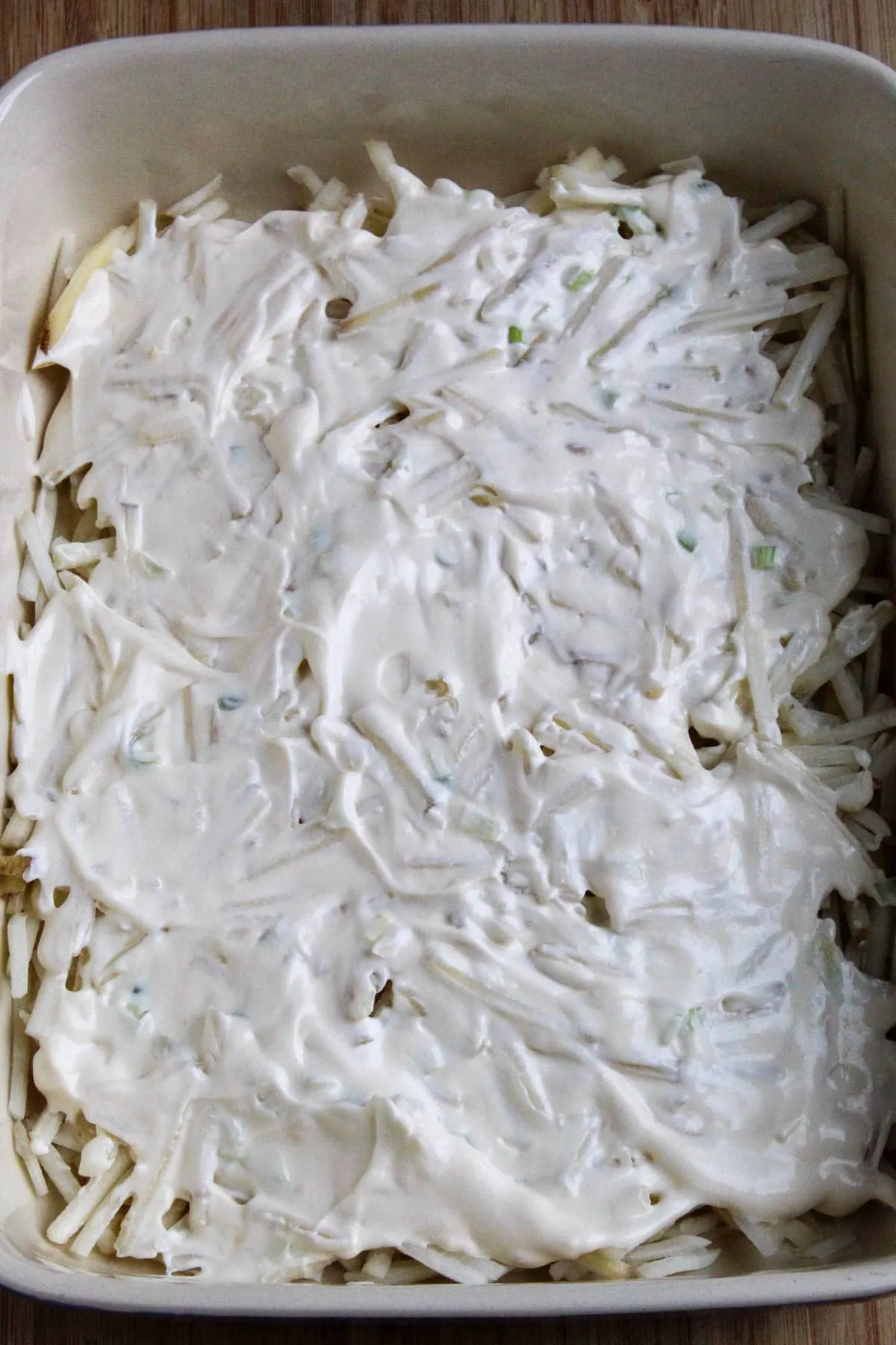 Process photo showing layer of sour cream mixture over frozen hash browns.